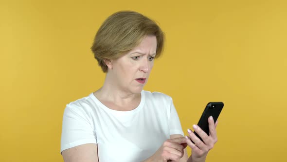 Old Woman Reacting to Loss and Using Smartphone Isolated on Yellow Background
