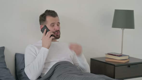 Angry Man Talking on Smartphone in Bed