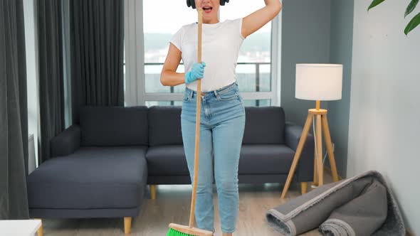 Woman in Headphones Cleans the House and Have Fun Singing with a Broom Like a Star at a Concert