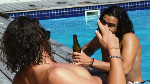 Happy friends interacting with each other while enjoying drinks by poolside