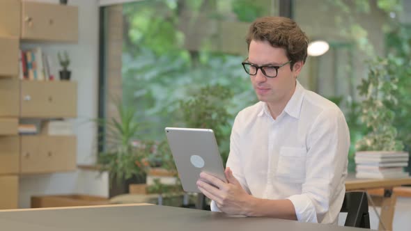 Young Man Reacting to Loss on Tablet While Sitting in Modern Office