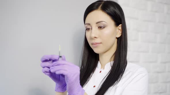 A beautiful cosmetologist with long hair checks the syringe with an injection