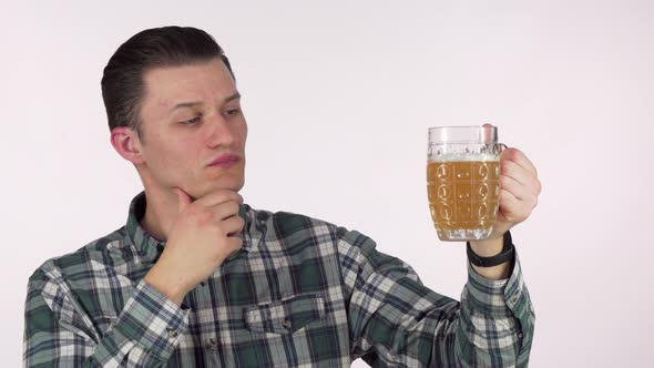 Young Man Rubbing His Chin Thoughtfully, Examining Beer in a Mug