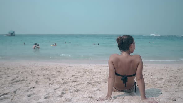 Woman Sits on Beach and Sunbathes Looking at Blue Ocean