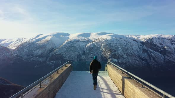 Following behind person walking towards edge and sitting down at Stegastein viewpoint during sunrise