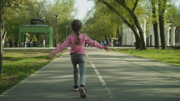 Happy Little Girl Runs Waving Hands Along Road in Garden