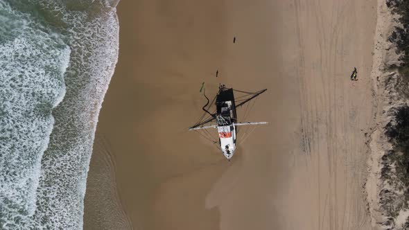 High drone view looking down at a fishing trawler recently washed up on a deserted beach with waves