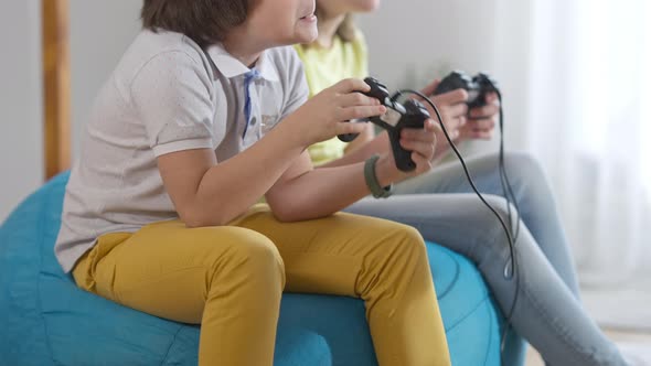 Carefree Unrecognizable Children Playing Video Games Sitting on Comfortable Bag Chair Indoors