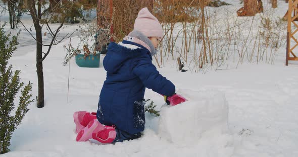 Cute Girl Builds and Plays in the Snow in the Forest