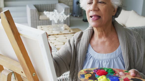 Portrait of african american senior woman smiling while painting on canvas at home