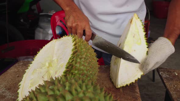 Asian man cutting and peeling durian with knife and wearing glove. Opening the king of fruits at asi