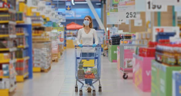 Young Woman Rolls a Grocery Cart with Goods in a Supermarket