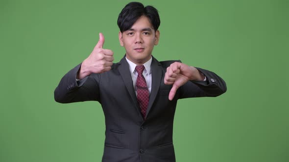 Young Confused Asian Businessman Giving Thumbs Up and Down