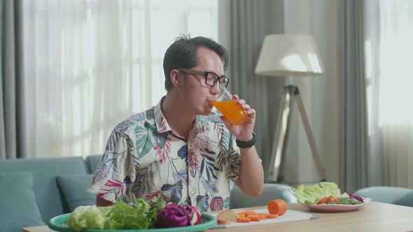 Asian Man Enjoys Drinking Orange Juice While Preparing Healthy Food At Home