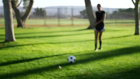 A female soccer player kicking a football to her teammate on a grass sport field.