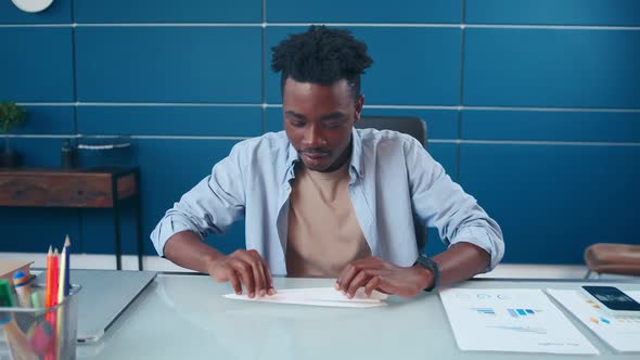 Young African American Man Launches Paper Plane Made Sits at Table in Office