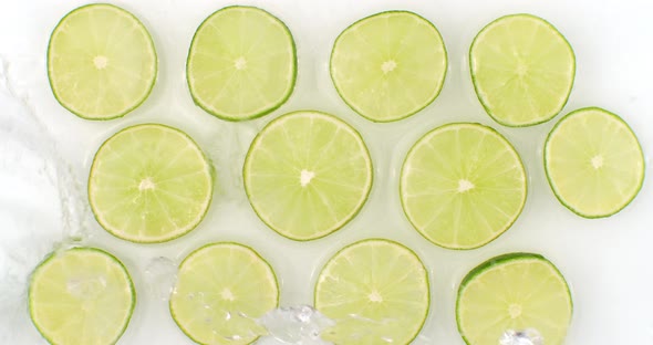 On a White Background, Sliced Pieces of Lime Are Sprinkled with Water. Juicy Fresh Lime in Slow