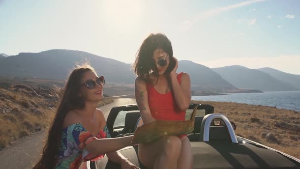 Two Girls Using Map Sitting on a Trunk of Cabrio
