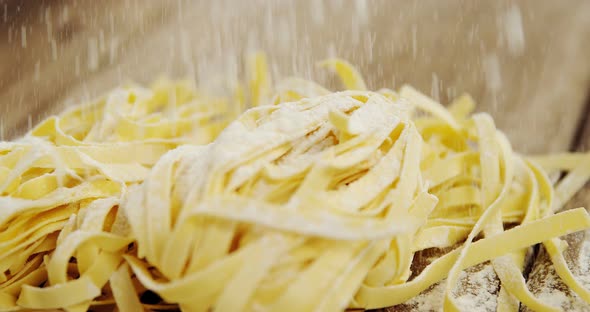 Close-up of flour springing on uncooked tagliatelle pasta on wooden background