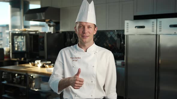 Professional kitchen portrait: Male Chef showing thumbs up and smiling