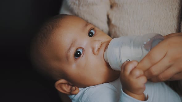 Close Up Adorable Dark Skin Baby Drinking His Milk From the Bottle in Mothers Hands