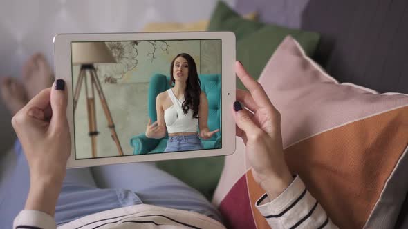 Young Woman at Home Lying on a Couch Watching Blogger Video on a Tablet