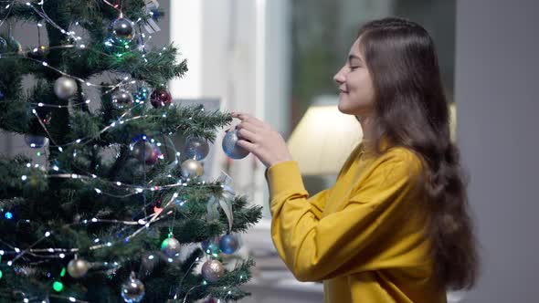 Side View of Young Charming Woman Making a Wish Hanging Decoration on New Year Tree
