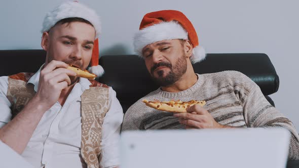 Lovely Gay Male Couple with Christmas Hats Eating Pizza and Watching Movies on the Christmas Eve