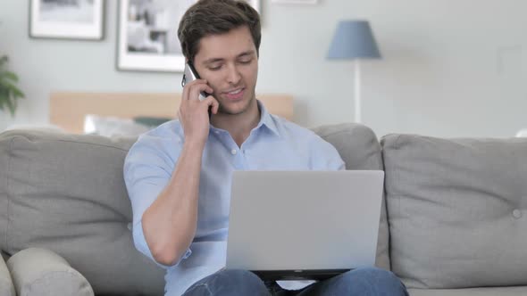 Happy Young Man Talking on Phone and Working on Laptop