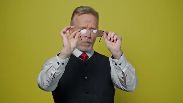 Senior man holds new glasses isolated in yellow studio. 