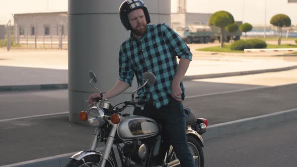 Portrait of Man Motorcyclist Smokes a Cigarette While Sitting on a Motorcycle at Street