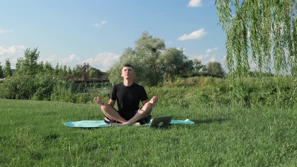 Man meditating outdoors with online guiding on laptop