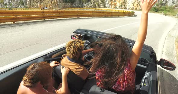 Group of friends driving on the road along the coast in red convertible