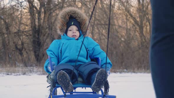 Parent Carrying Happy Little Boy on Sled in Winter. Toddler Kid Enjoying a Sleigh Ride. Outdoor Fun