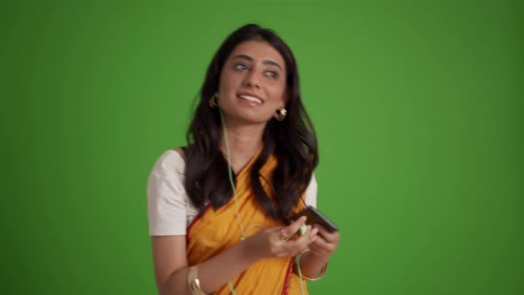 Positive traditional Indian woman listening music in headphones and dancing