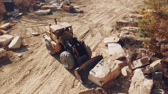 professional equipment with a bucket is turning over a stone and raising it near sandy quarry