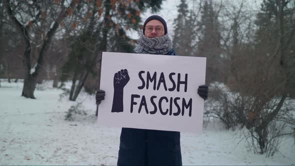 Man is Holding a Sign that Says Smash Fascism with a Black Fist on the Side.
