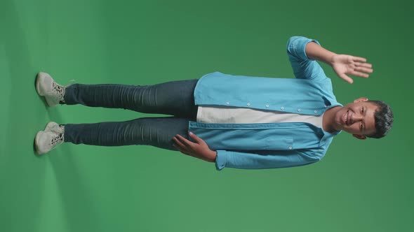 The happy young Asian man waving hand while standing on green screen in the studio