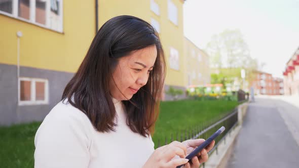 Asian woman with black straight hair and happy face. Standing and using her smart phone