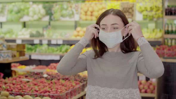 Young Serious Woman Putting on Face Mask in Supermarket. Portrait of Brunette Caucasian Girl Buying