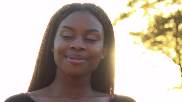 Young Beautiful Black Woman Smiles To Camera in Park During Sunset with Sun Rays