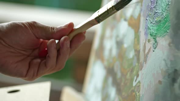 Closeup of a Brush Dipping Into Paint and a Man's Hand Painting a Picture alt