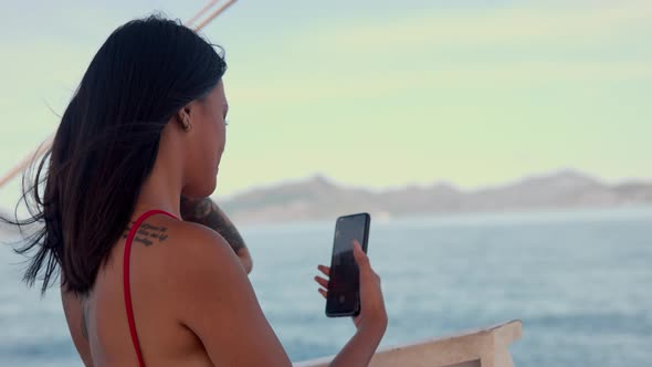 Woman In Red Swimsuit Using Smartphone For Selfie On Boat