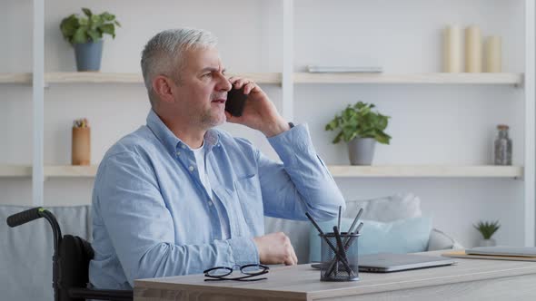 Discontented Disabled Man Talking On Phone Sitting In Wheelchair Indoor