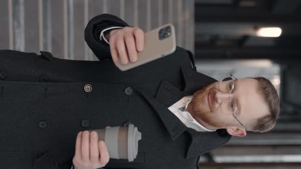 Vertical Video of the Businessman in Formal Suit Using Smartphone and Holding Cup of Coffee in Hands