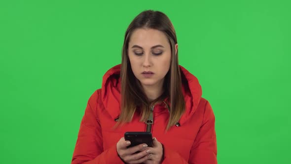 Portrait of Lovely Girl in a Red Down Jacket Is Texting on Her Phone. Green Screen