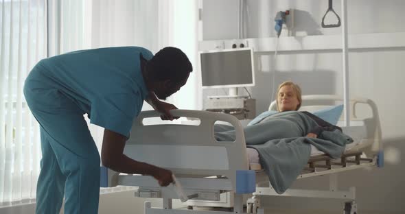 Afroamerican Man Nurse Adjusting Bed for Woman Patient