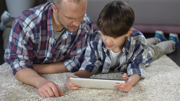 Boy Using Interactive Application on Tablet With Help of Father, Family Time