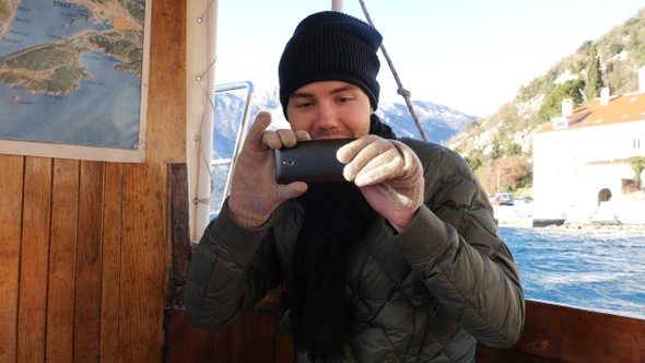 Handsome smiling young man tourist recording a video on a boat.