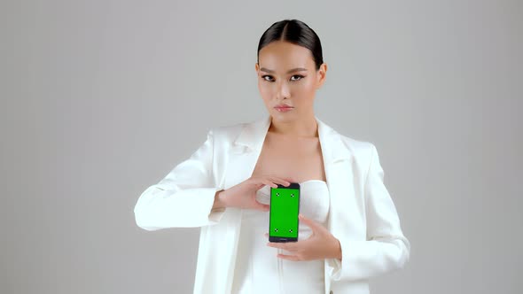 Beautiful Asian businesswoman showing smartphone with green screen